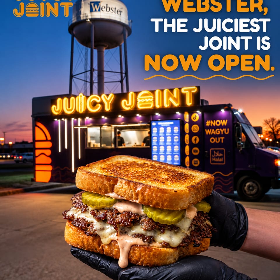 Gloved hands hold a loaded toasted sandwich before Juicy Joint’s illuminated food truck at dusk.