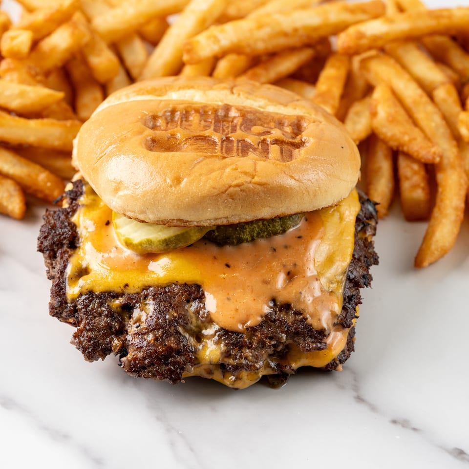 Double cheeseburger with pickles and special sauce served alongside golden French fries on a white marble surface.